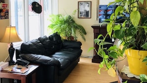 A living room with a black leather sofa, a wooden coffee table, a lamp, a potted plant, and a framed picture on the wall.
