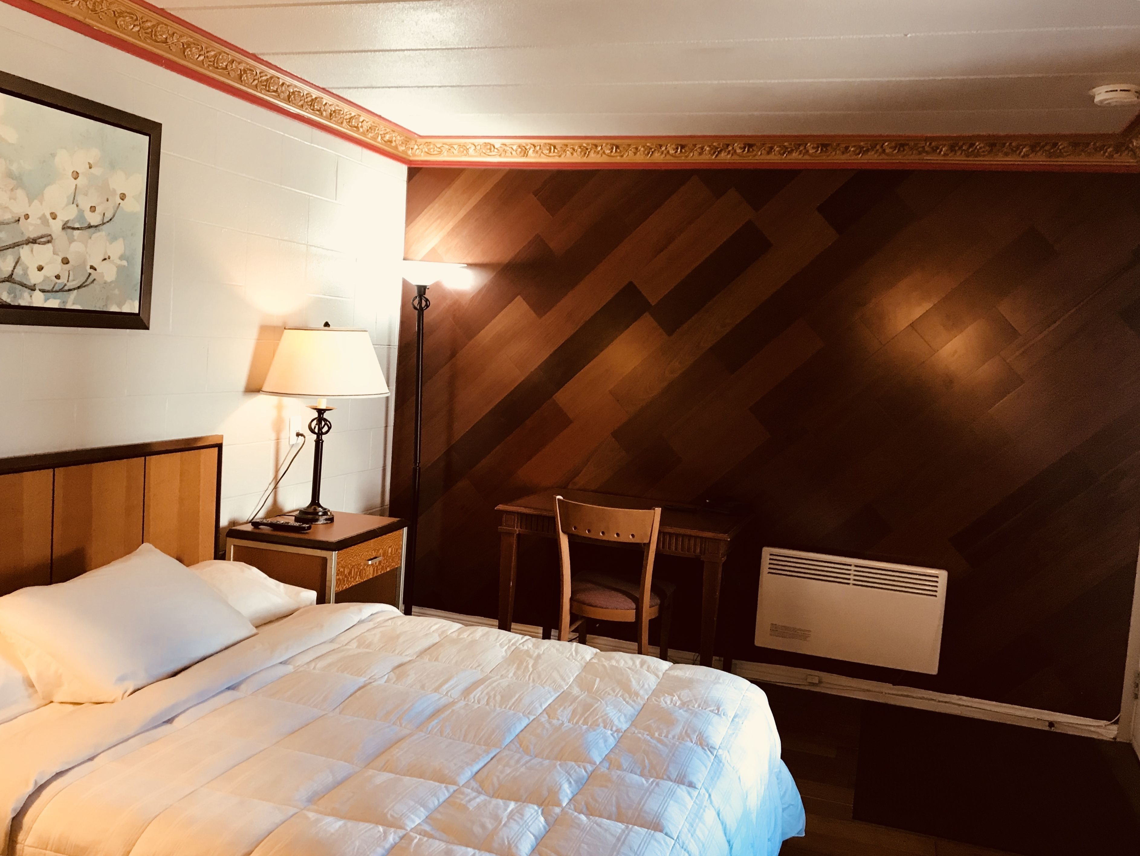 A hotel room with a bed, a nightstand with a lamp, a chair, and a radiator.