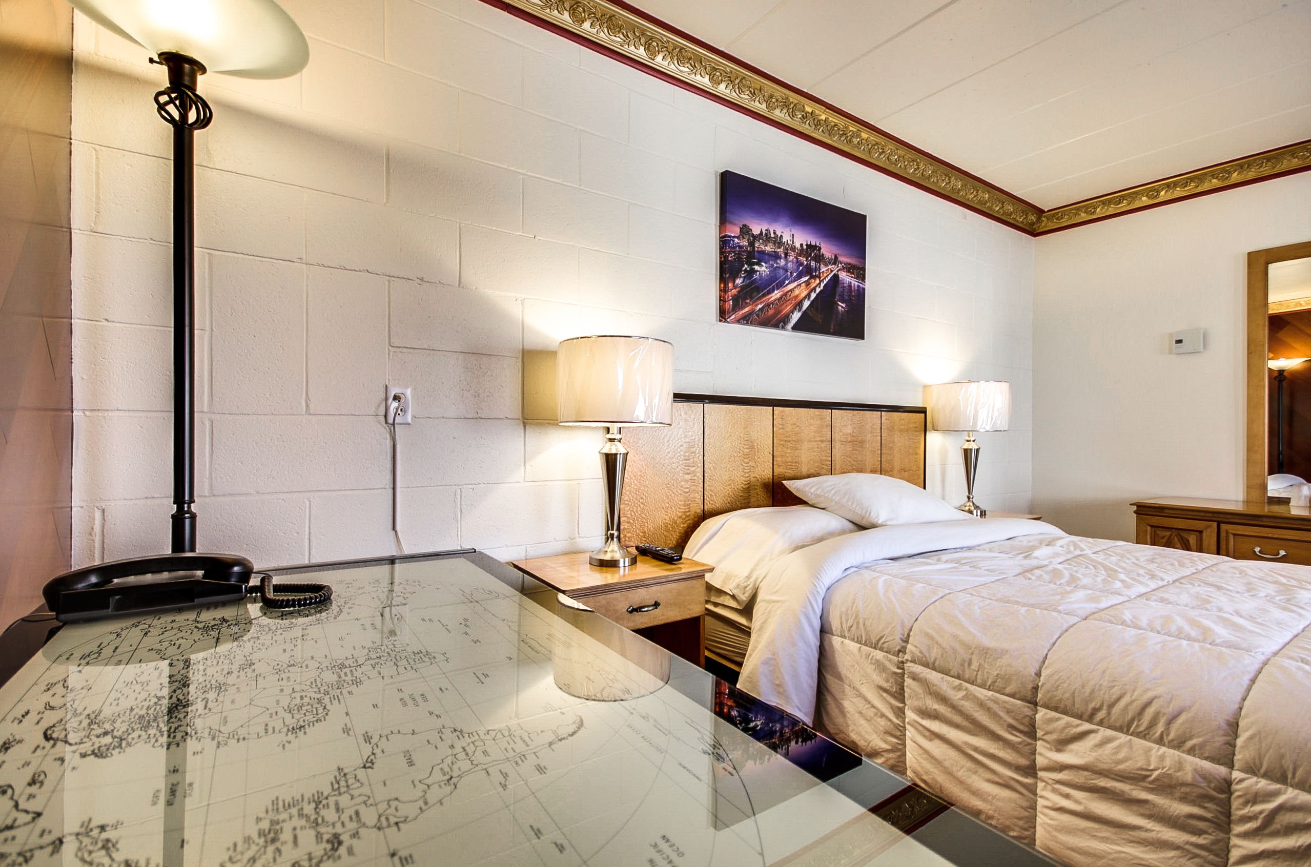 A hotel room with a bed, two bedside lamps, a nightstand with a lamp, a telephone, and a map on the table.
