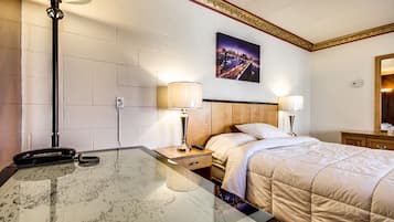 Habitación de hotel con cama, dos lámparas de noche, mesita de noche con lámpara, teléfono y un mapa sobre la mesa.