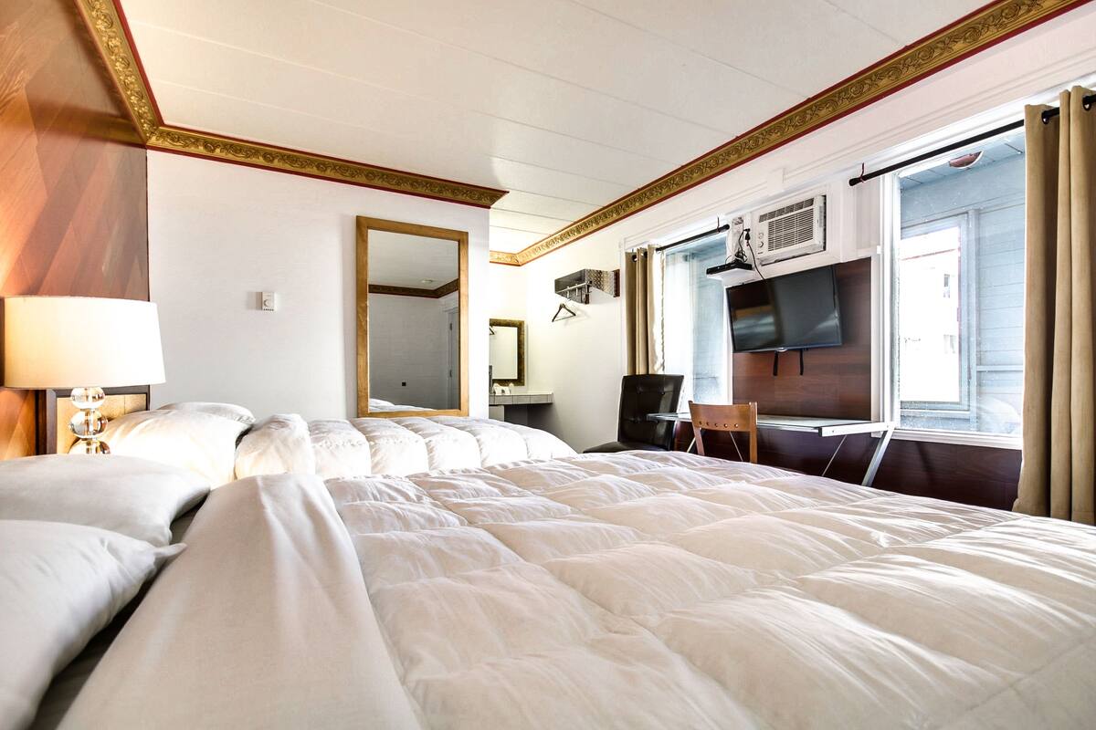 A hotel room with a large bed, a desk with a chair, a television, and a window with curtains.