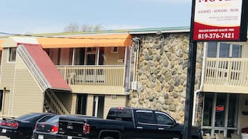 Un motel con fachada de piedra, un toldo rojo y un cartel que lo anuncia como lugar para trabajadores de la construcción. Dos camionetas GMC negras están estacionadas frente a él.