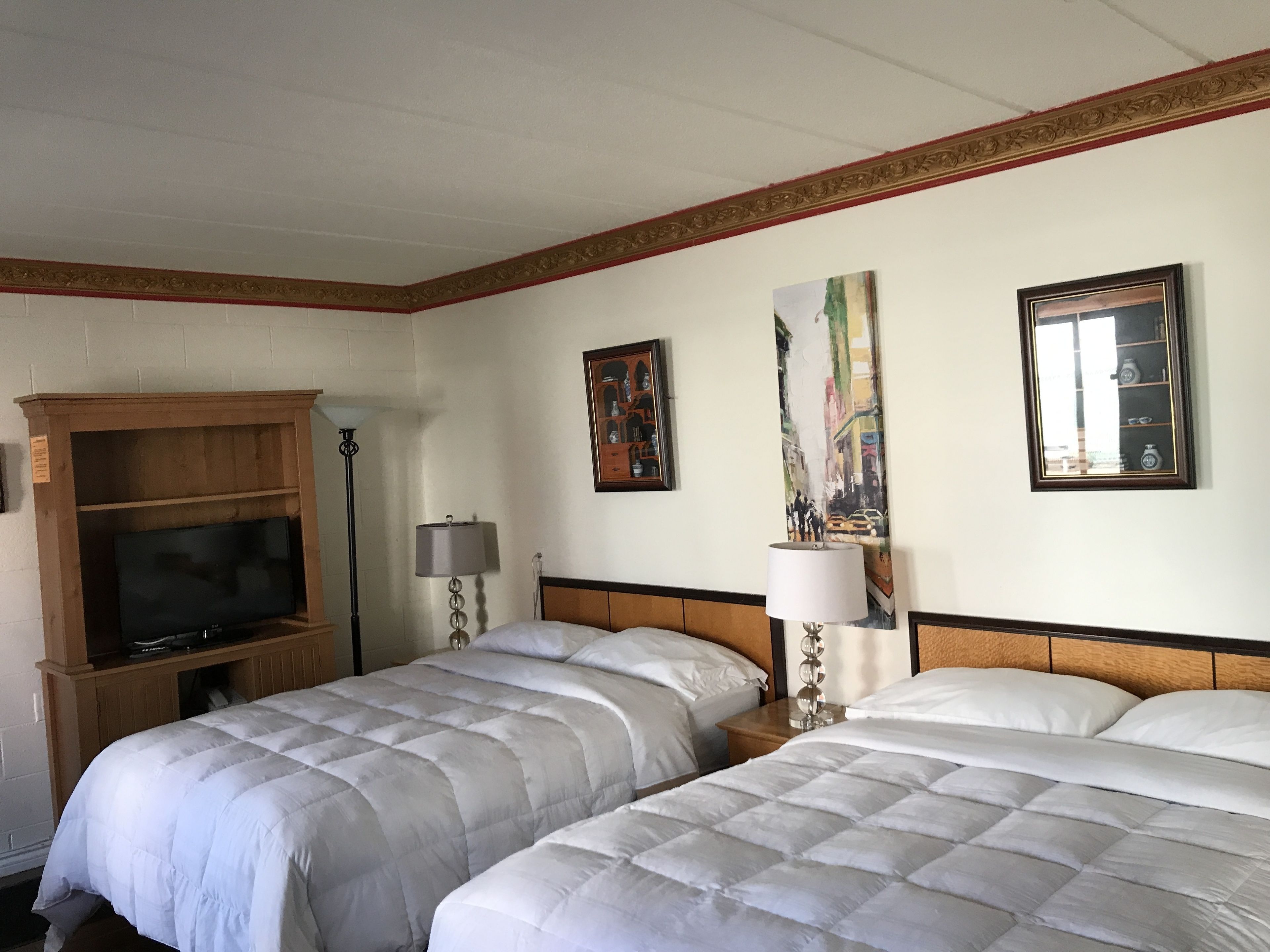 A hotel room with two beds, a TV, a lamp, and artwork on the walls.