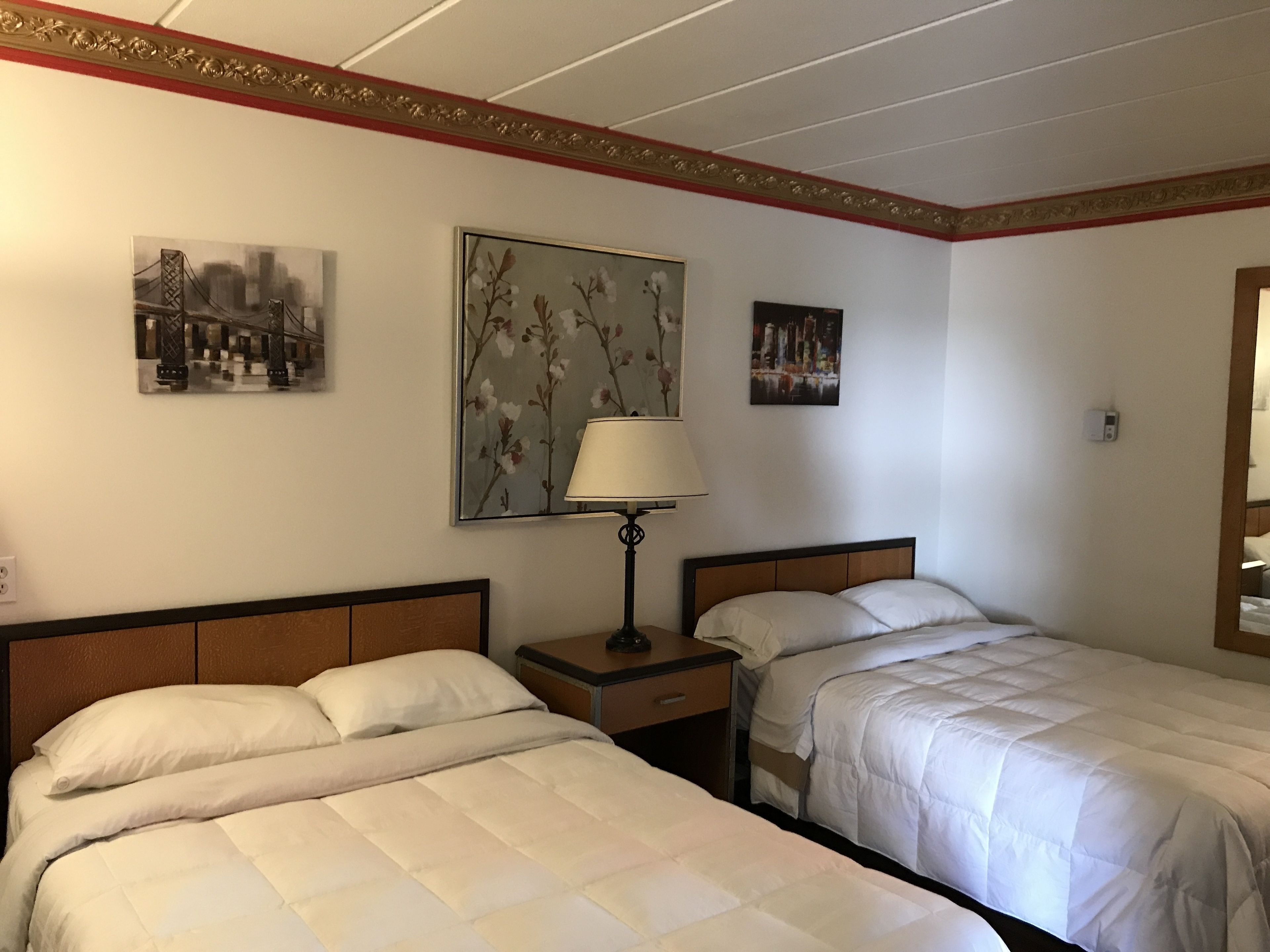A hotel room with two beds, a nightstand, a lamp, and wall art.