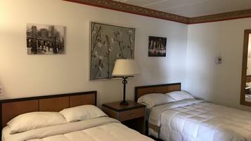 A hotel room with two beds, a nightstand, a lamp, and wall art.