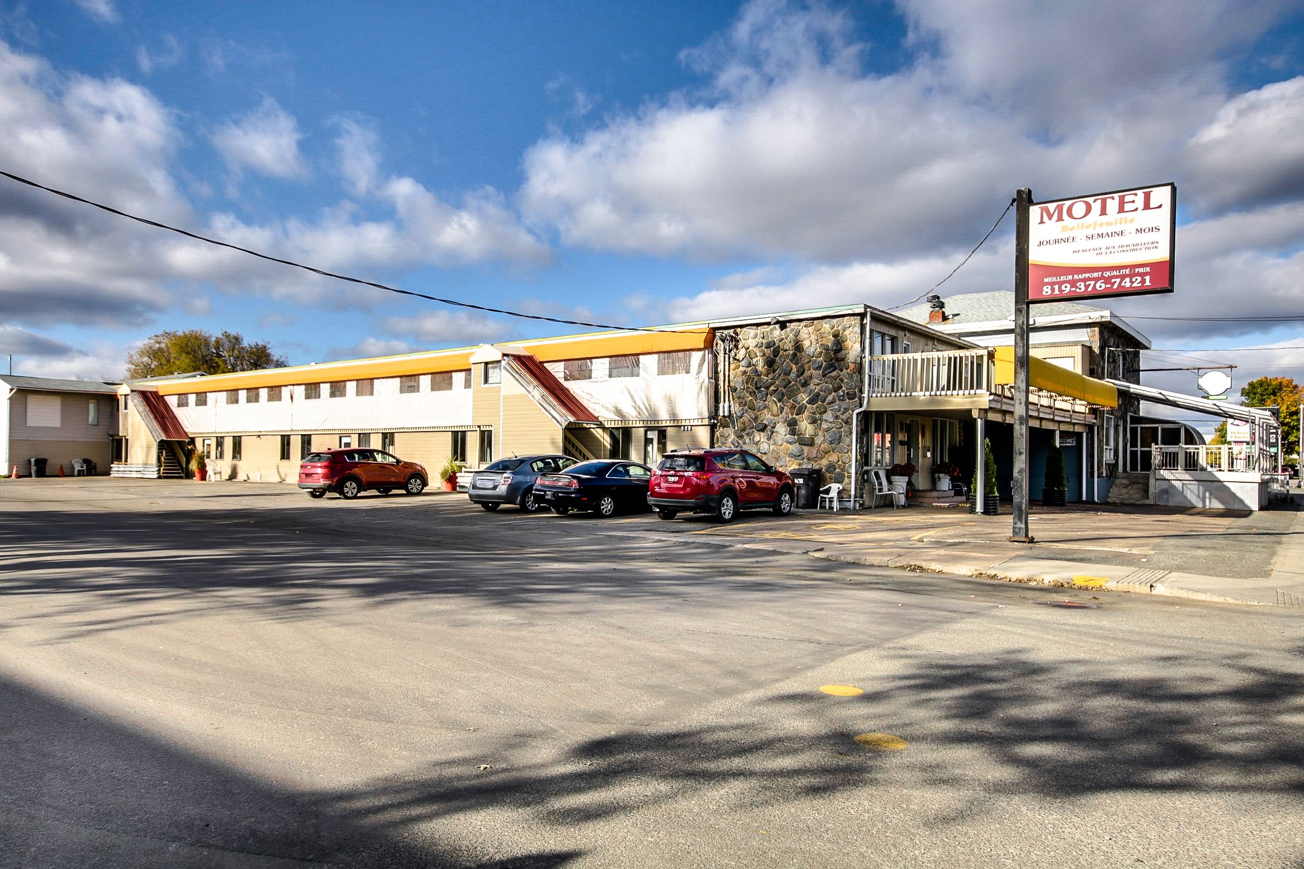 A motel with a signboard, a parking lot with several cars, and a building with a yellow and white facade.