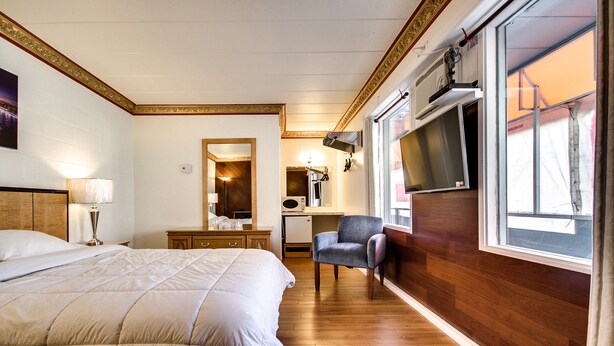 A hotel room with a large bed, a desk with a chair, a TV, and a window with curtains.
