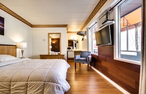 Habitación de hotel con una cama grande, un escritorio con silla, televisión y ventana con cortinas.