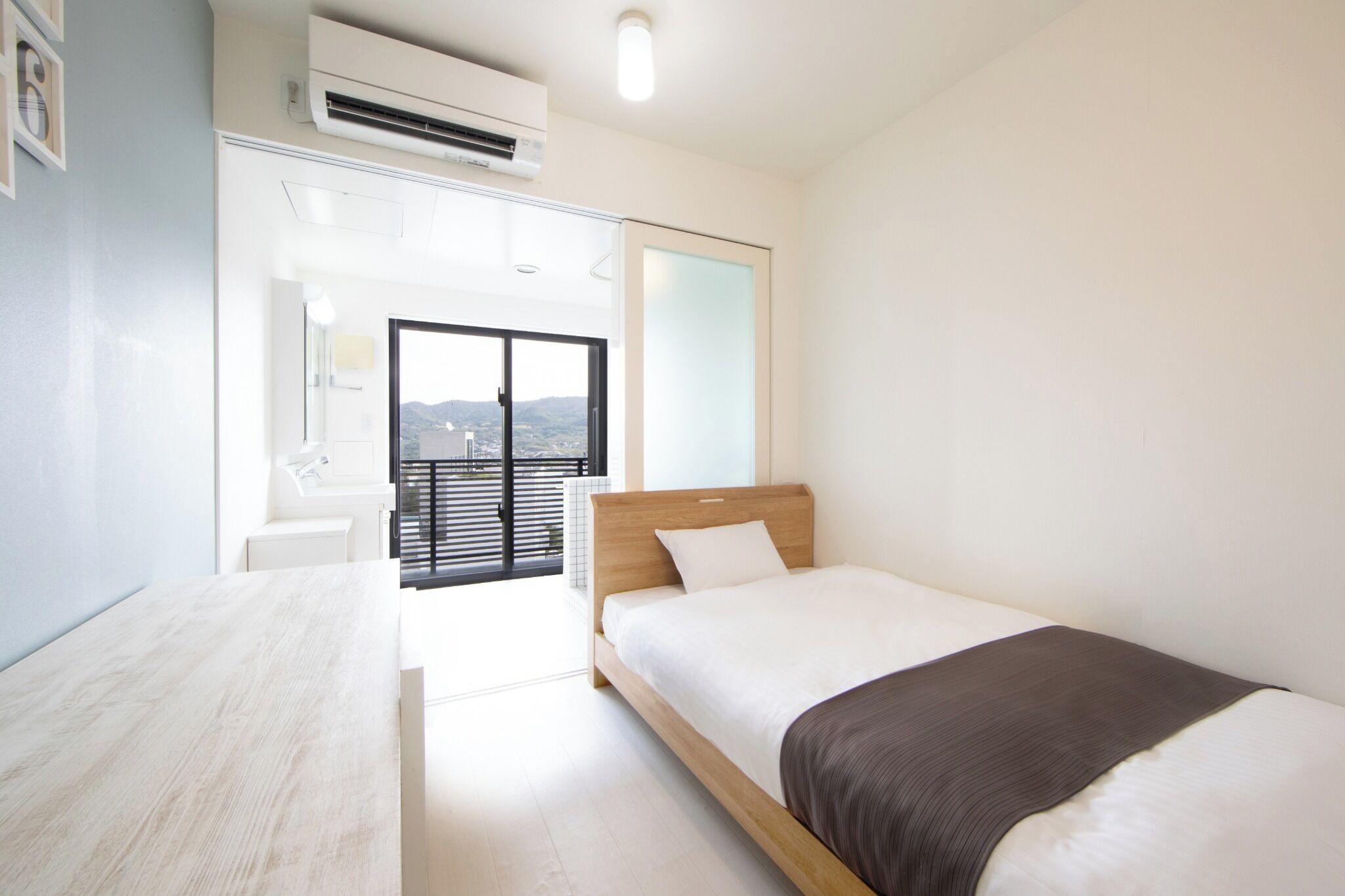 Un dormitorio moderno con cama, mesita de noche de madera, ventana grande y aire acondicionado.
