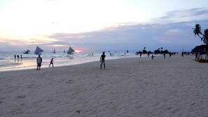 A beach with people, sailboats, and a sunset.