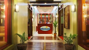 A hotel reception area with a reception desk, two receptionists, and potted plants.