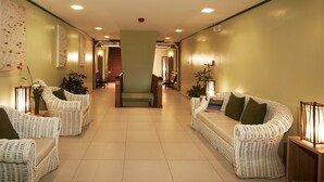 A hallway with wicker sofas and chairs, a staircase, and a wooden table with a lamp.