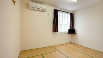 A room with tatami flooring, a mounted air conditioner, a window with curtains, and a flat-screen TV on a shelf.