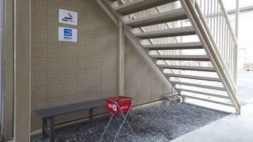 A staircase with a beige wall, a red trash bin, and two signs indicating smoking and smoking policy.