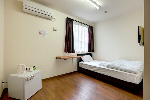 A small, clean room with a single bed, a desk with a kettle and cups, and an air conditioner on the wall. - Hotel Southern Village Okinawa (Kitanakagusuku)