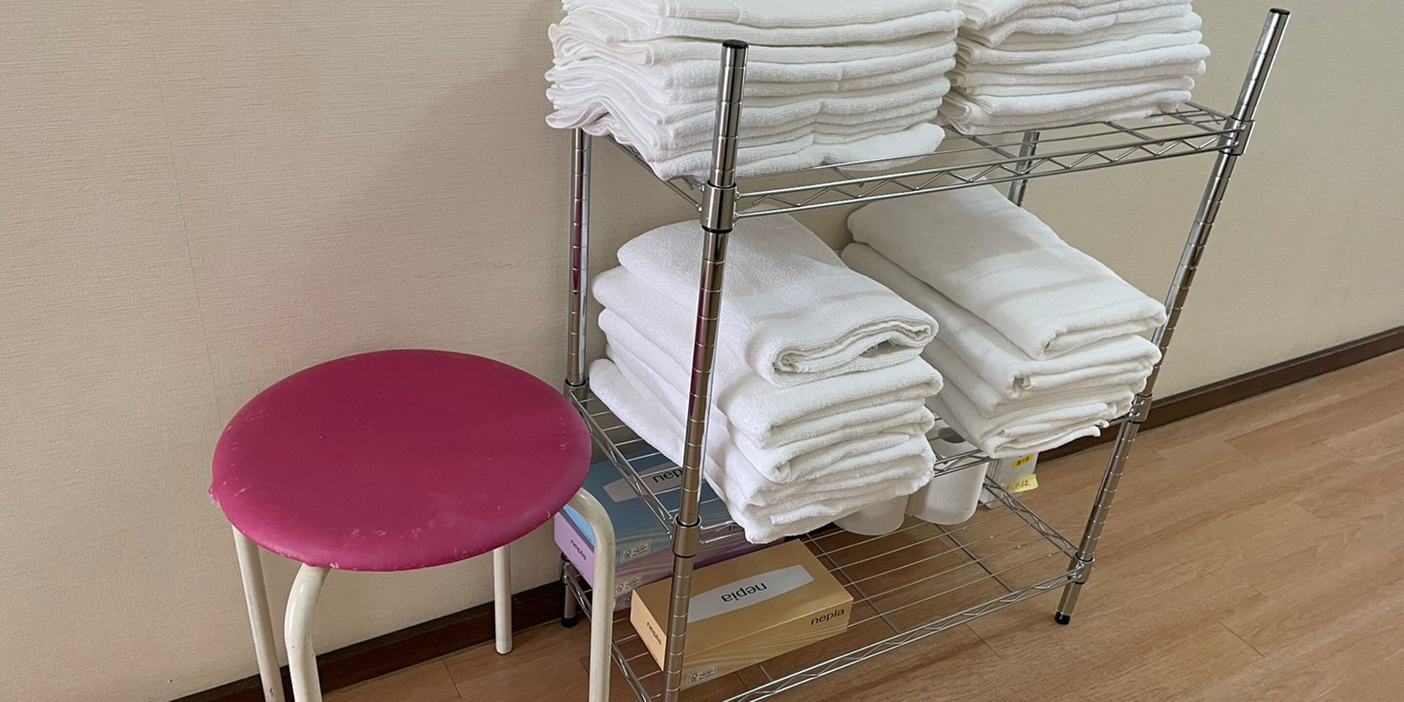 A metal shelf with folded white towels and a pink stool beside it.