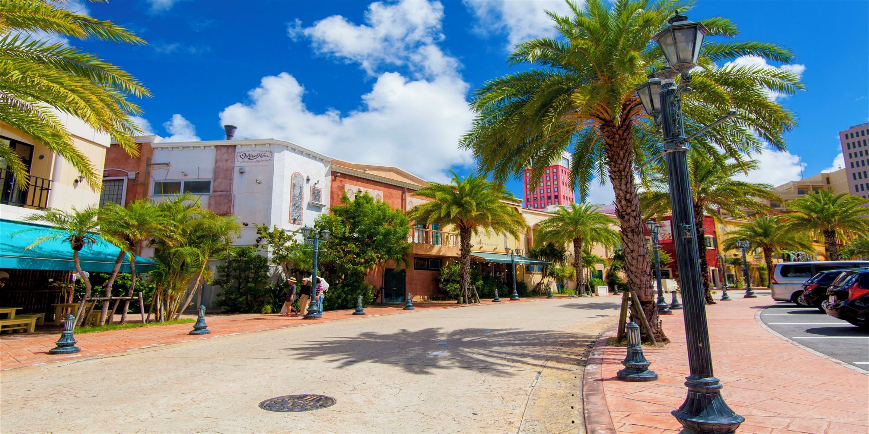 A street with palm trees, a building with a sign, and parked cars.