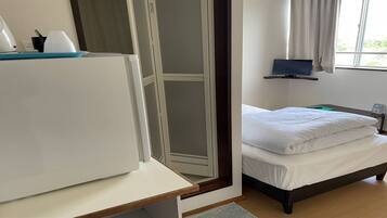 A hotel room with a bed, a desk with a computer, a TV, and a window with curtains.