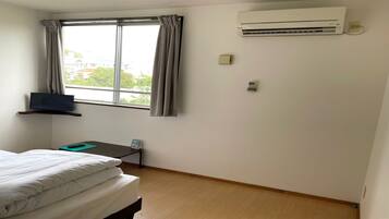 A hotel room with a bed, a desk with a laptop, an air conditioner, and a window with curtains.