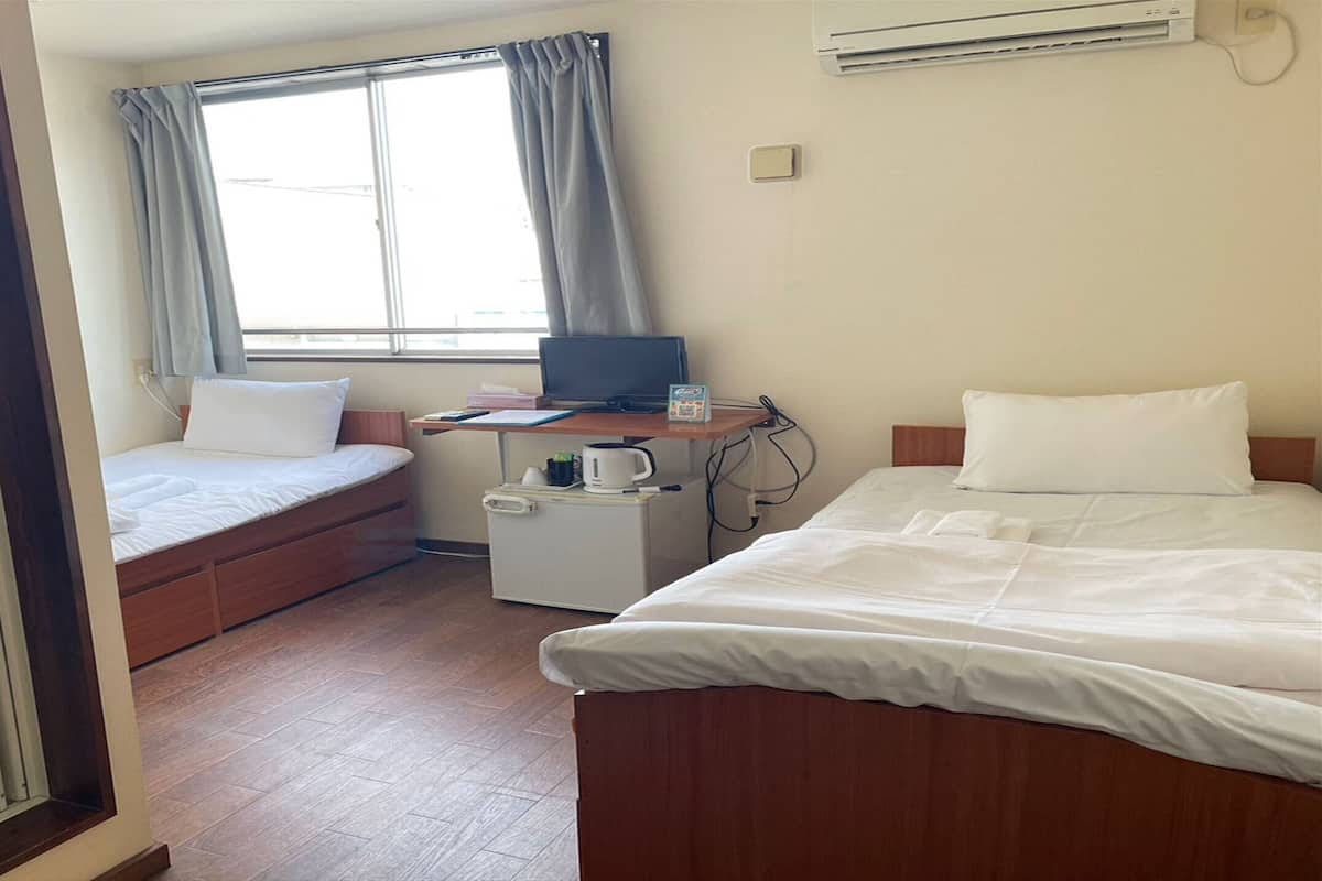 A hotel room with two beds, a desk with a computer, a small fridge, and a window with curtains.