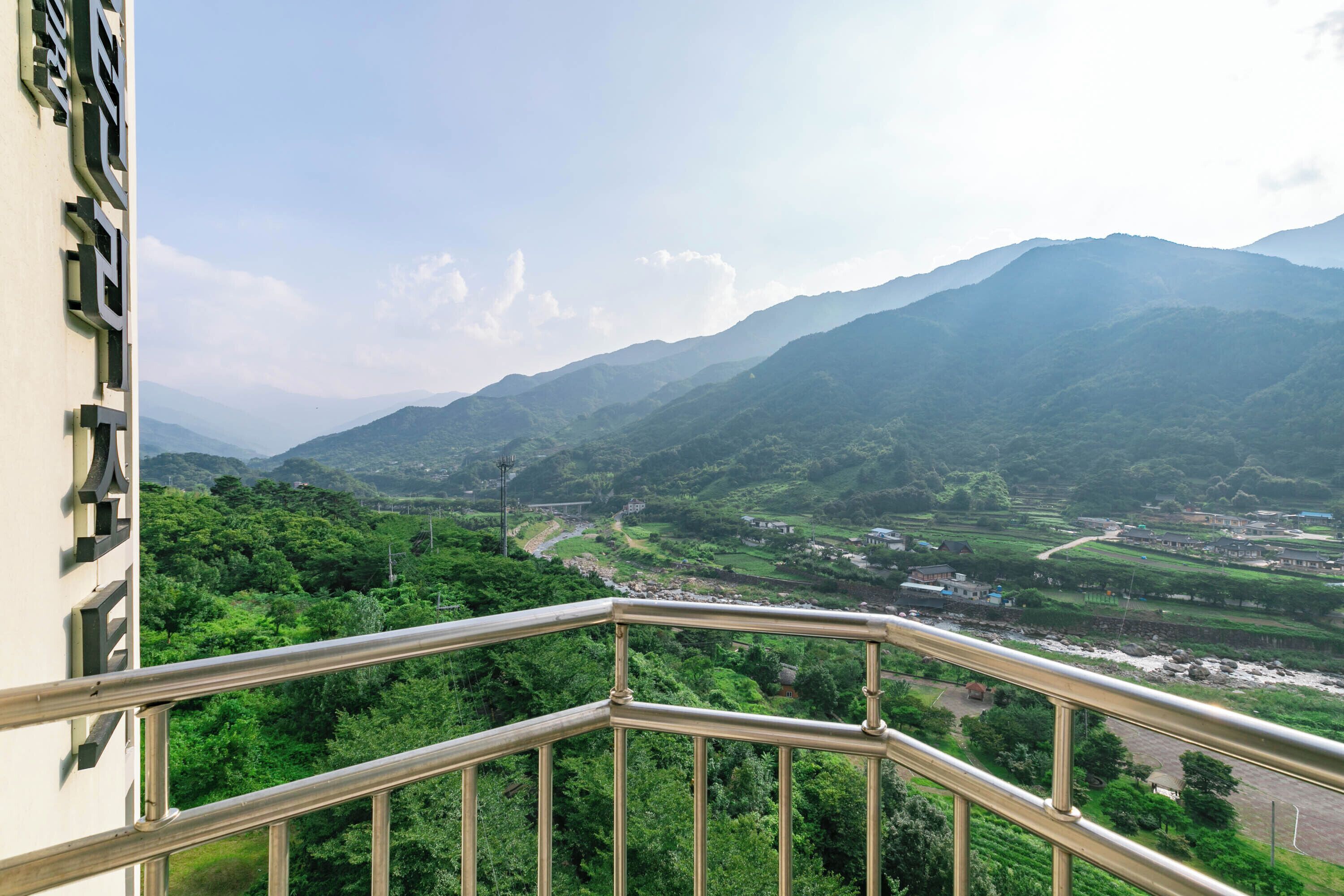 A balcony with a metal railing overlooking a mountainous landscape with greenery and a river.