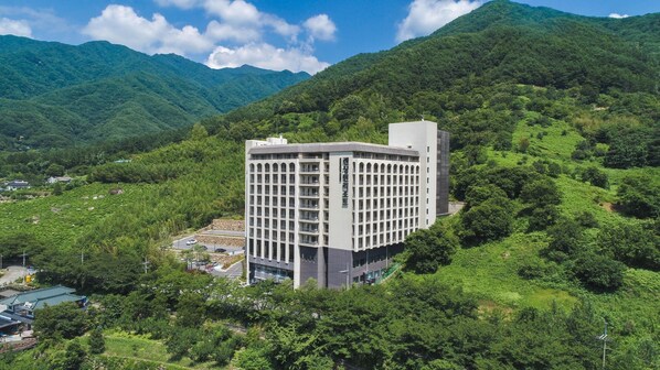 A modern multi-story building with a flat roof, surrounded by lush green hills and a clear sky. - Kensington Resort Jirisan Hadong (Hadong)