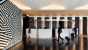 Un moderno vestíbulo de hotel con una recepción, un diseño de pared geométrico y un piso de madera pulida.