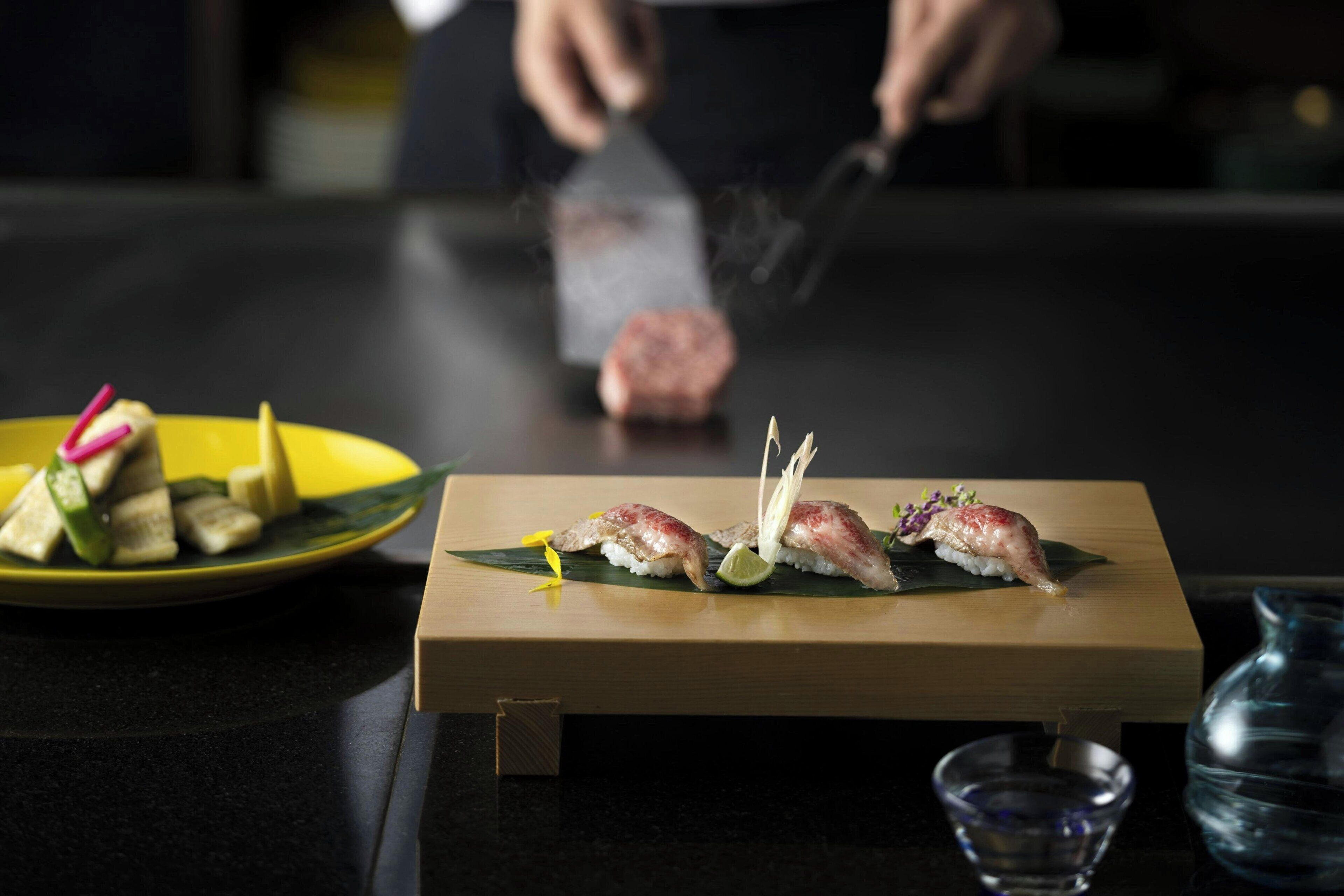 A sushi dish on a wooden tray with a small bowl and a glass of water nearby.