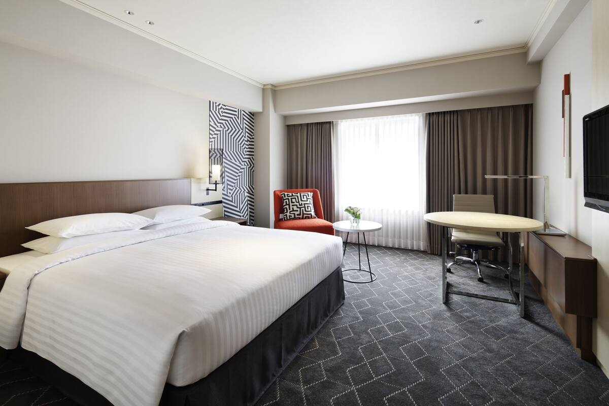 Habitación de hotel con una cama grande, un escritorio, una silla, un televisor y una ventana con cortinas.