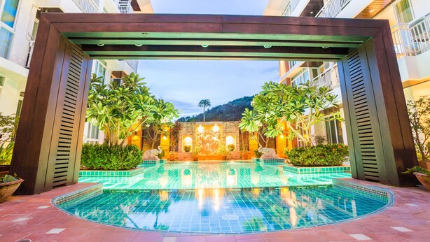 A pool area with a wooden pergola, surrounded by lush greenery and a decorative wall. - Arisara Place (Koh Samui)