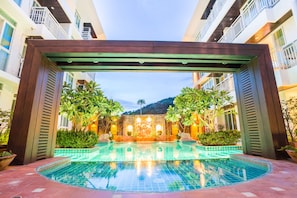 A pool area with a wooden pergola, surrounded by lush greenery and a decorative wall.