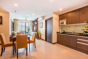 A modern kitchen with dark wood cabinets, a microwave, and a sink. There is a dining area with a table and chairs, and a ceiling fan above.