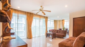 A spacious living room with a ceiling fan, a sofa, a coffee table, and a wooden reception desk with a telephone. - Arisara Place (Koh Samui)