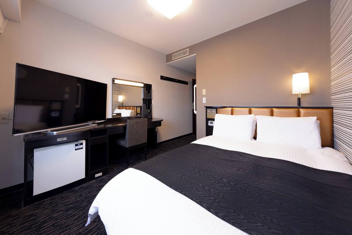 Ein Hotelzimmer mit einem Bett, einem Schreibtisch mit Fernseher, einem Spiegel, einem Nachttisch und einer Lampe.