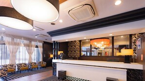 Un espace d’accueil d’hôtel comprenant un comptoir, des sièges et un grand miroir.
