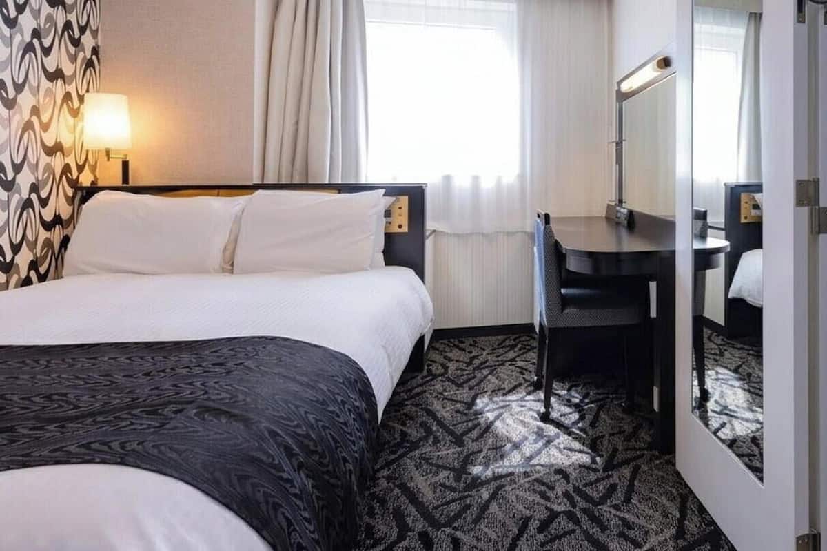 A hotel room with two beds, a desk, a mirror, and a patterned carpet.