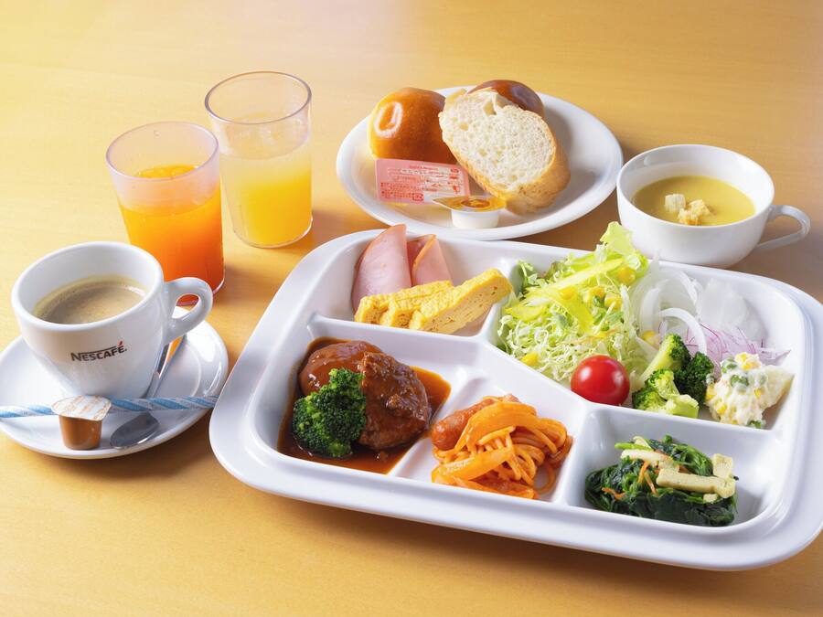 A meal tray with various dishes including pasta, vegetables, and a bread roll. There are also two glasses of orange juice and a cup of coffee.