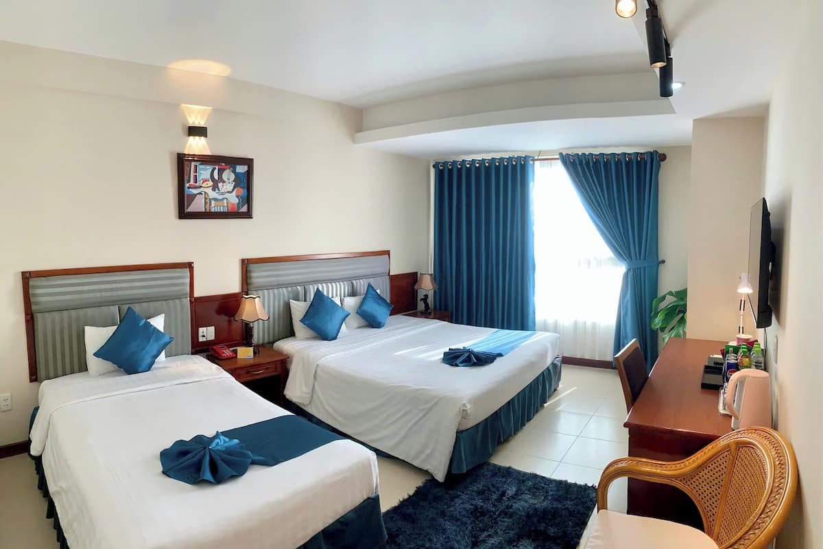 A hotel room with two beds, a desk, a chair, a TV, and a window with curtains.