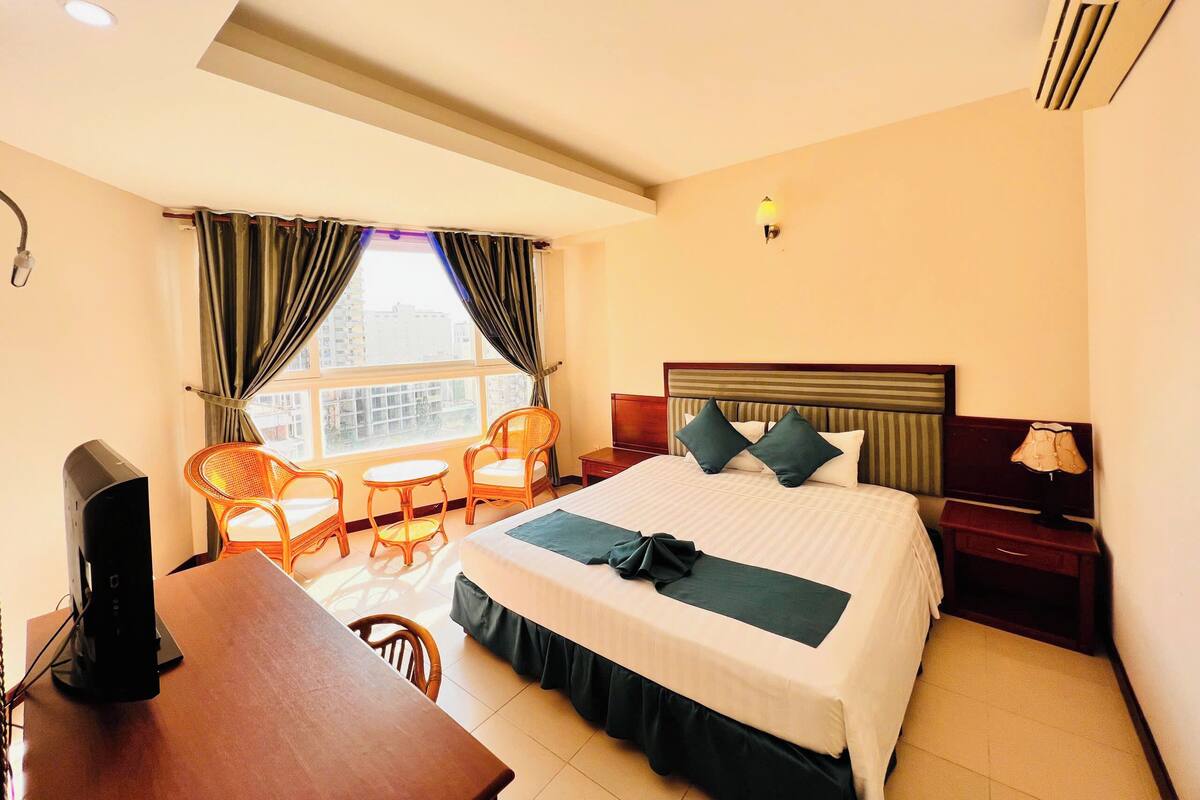 A hotel room with a bed, a desk, two chairs, a small table, and a window with curtains.