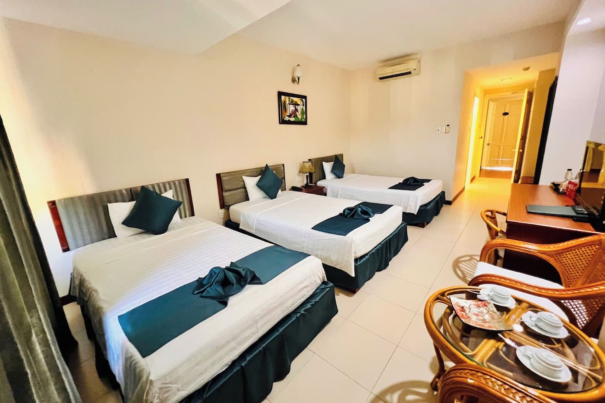 A hotel room with three beds, a dining table, and a small seating area with chairs.