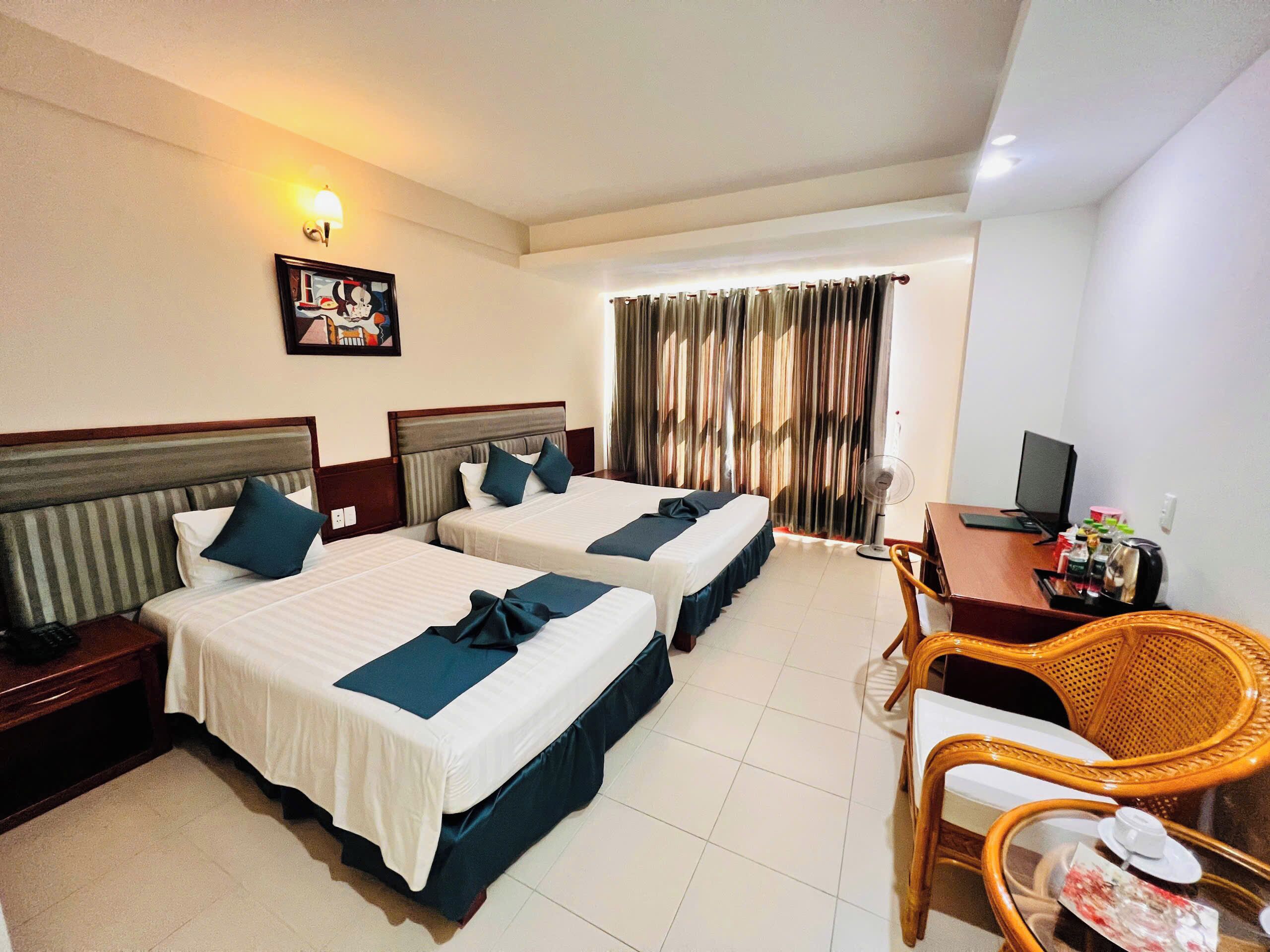 A hotel room with two beds, a desk with a computer, a chair, and a window with curtains.