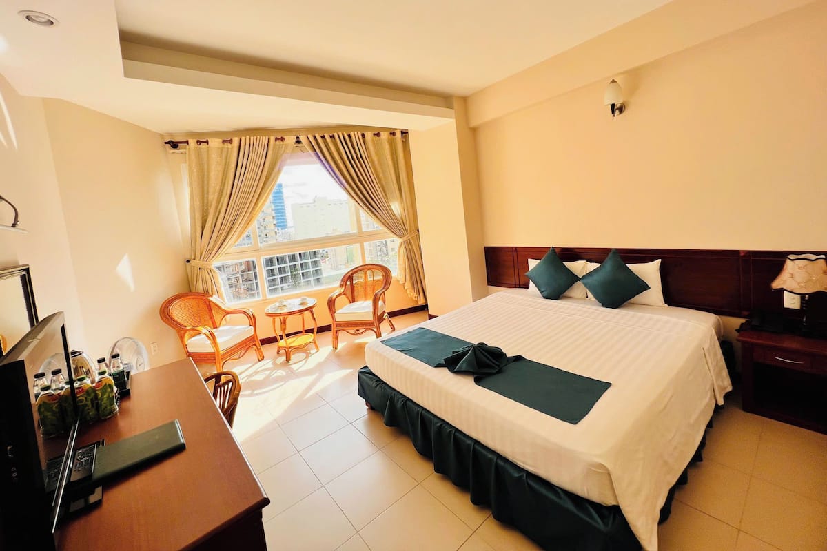 A hotel room with a bed, a desk, a chair, a small table, and a window with curtains.
