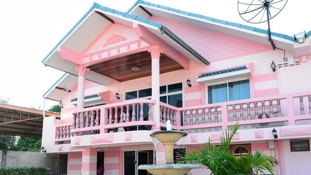 A two-story building with a pink and white color scheme, a balcony with a railing, and a fountain in the foreground. - Ky Dang Resort (Cha-am)