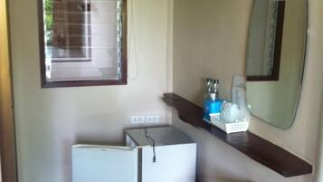 A compact bathroom with a white sink, a mirror, a small wooden stool, and a window with blinds.
