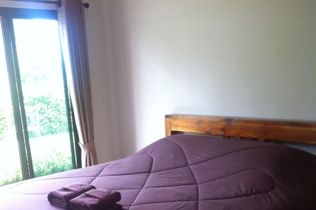 Una cama con cabecera de madera, colcha morada y una manta doblada al lado.