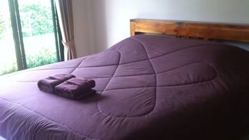 A bed with a wooden headboard, a purple bedspread, and a folded blanket on the side.