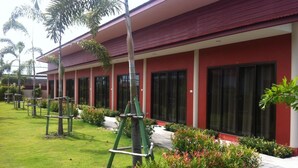 A red building with a covered walkway, surrounded by well-maintained grass and plants. - Dang Ky Resort (Cha-am)