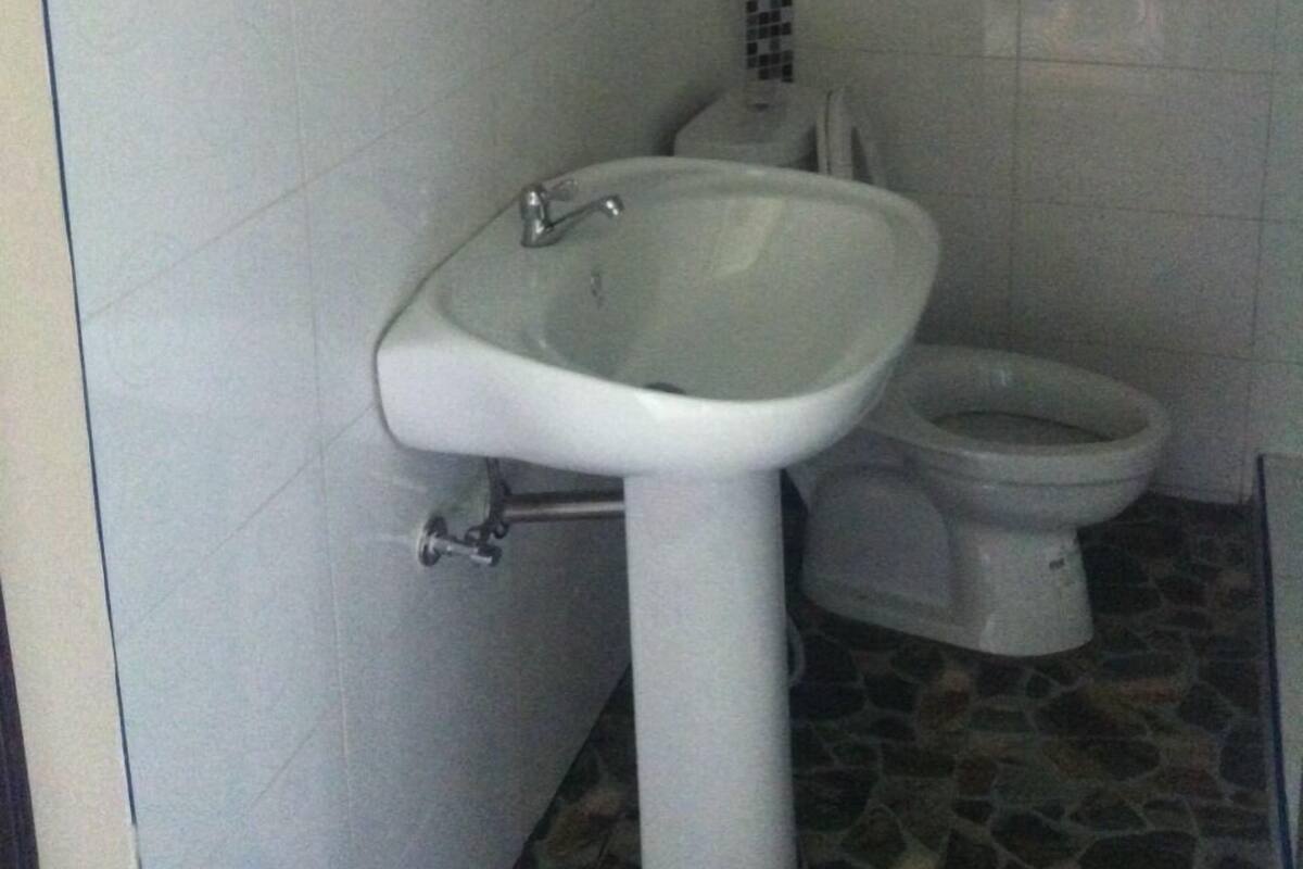 Un baño con lavamanos blanco, inodoro y un pequeño estante sobre el lavamanos.
