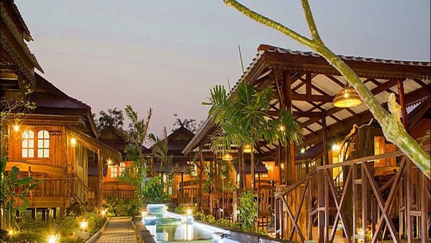 A resort with wooden buildings, a central water feature, and a well-lit pathway. - Dang Ky Resort (Cha-am)