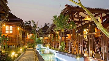 A resort with wooden buildings, a central water feature, and a well-lit pathway.